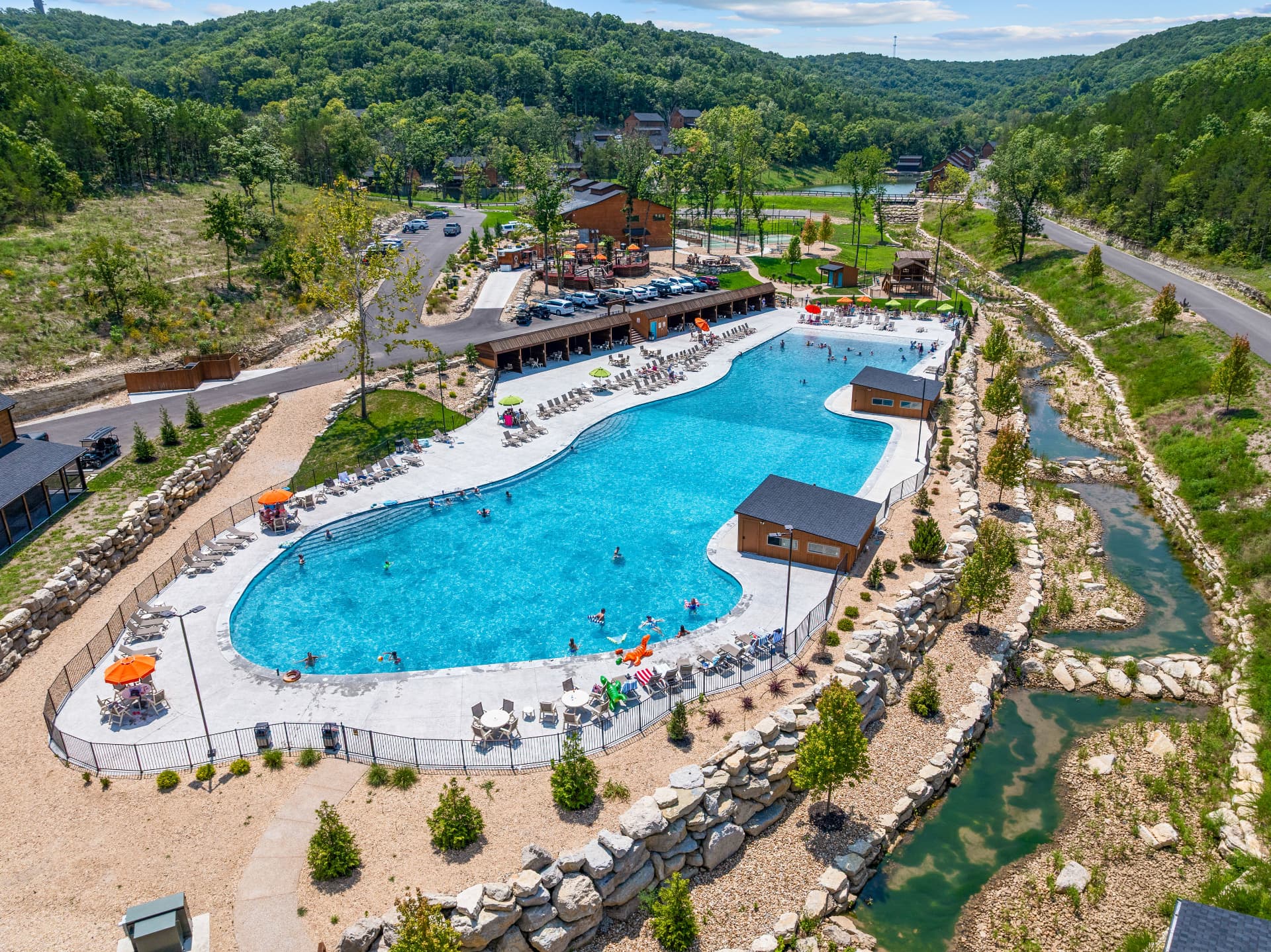 Aerial view of a resort pool and lazy river surrounded by wooded Ozark hills